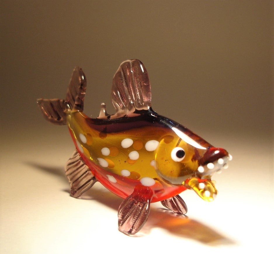 Close-up of a glass piranha figurine, highlighting its intricate details, including white round spots on its body.