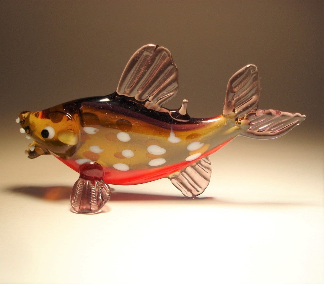 A side view of a glass piranha figurine, displaying its curved body and clear purple fins.