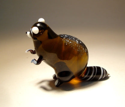 Side view of the glass raccoon figurine, highlighting its striped tail and fur texture.