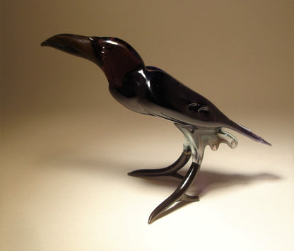 Side view of a glass raven crow figurine, highlighting its curved beak and intricately crafted wings