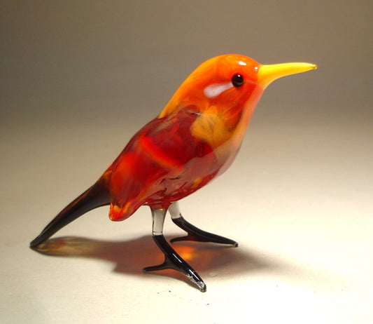 A vibrant glass red bird figurine standing upright, featuring a yellow beak and black tail.