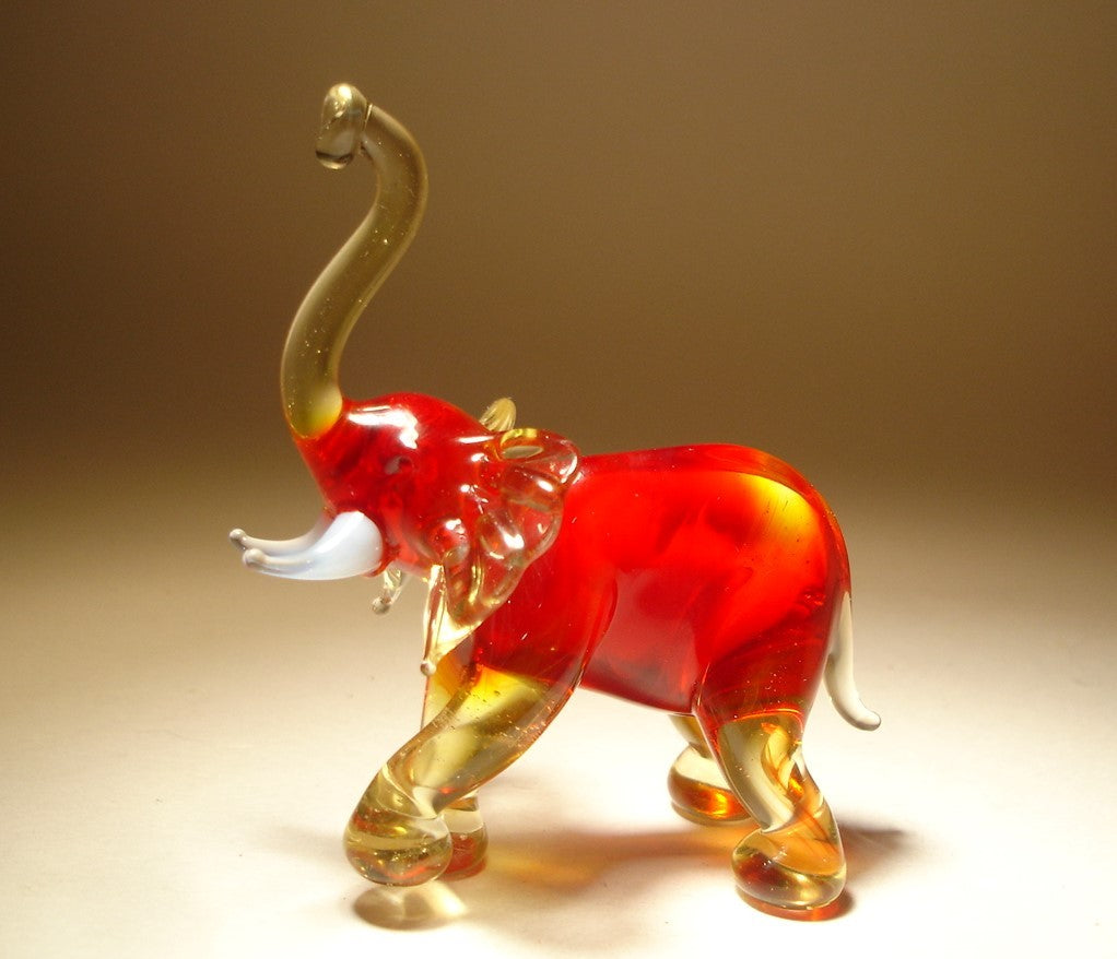 A side view of a red glass elephant figurine, highlighting its raised trunk and lifted left foot, with elegant detailing in its body and legs.