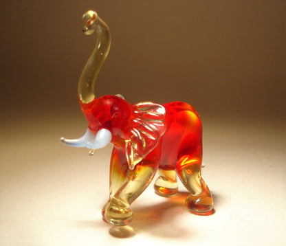 A handmade glass elephant in red with white tusks and clear light brown legs, trunk and ears.