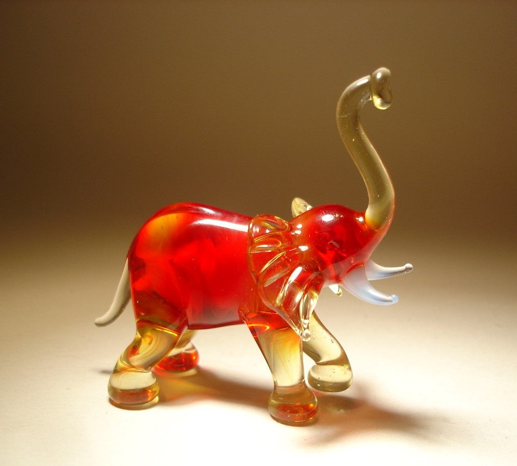 A front view of a red glass elephant figurine with its trunk raised high and left foot slightly lifted.