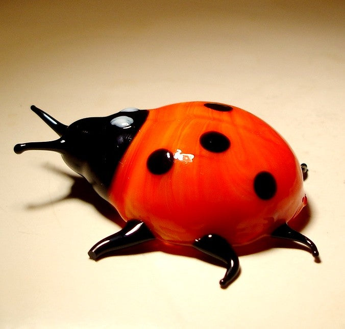 A cheerful glass ladybug figurine, featuring a glossy red body with black spots.