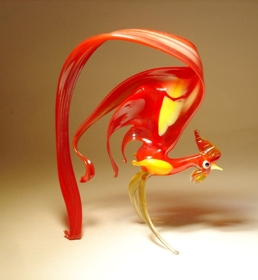 Side view of a glass rooster figurine with a curved long red tail with yellow spots on it and on the wings