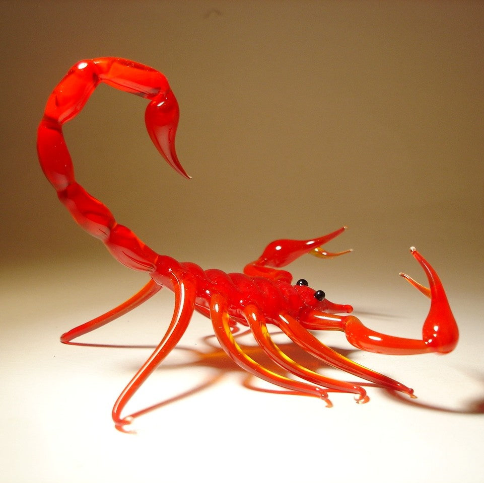 A side view of a red glass scorpion figurine, highlighting its sharp claws, detailed legs, and arched tail.