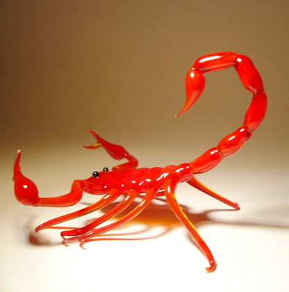 A front view of a red glass scorpion figurine with raised claws and a curved, segmented tail poised above its body.