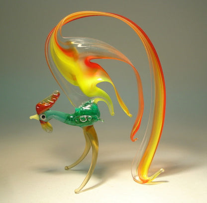 A side view of the glass rooster figurine, showcasing its gracefully arched tail in shades red and yellow.