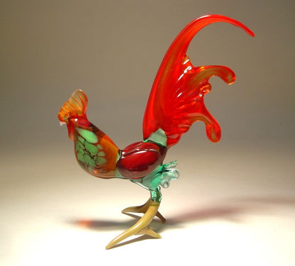 Another side view of an elegant glass rooster figurine with a vibrant red tail, featuring a detailed beak and ornate plumage.