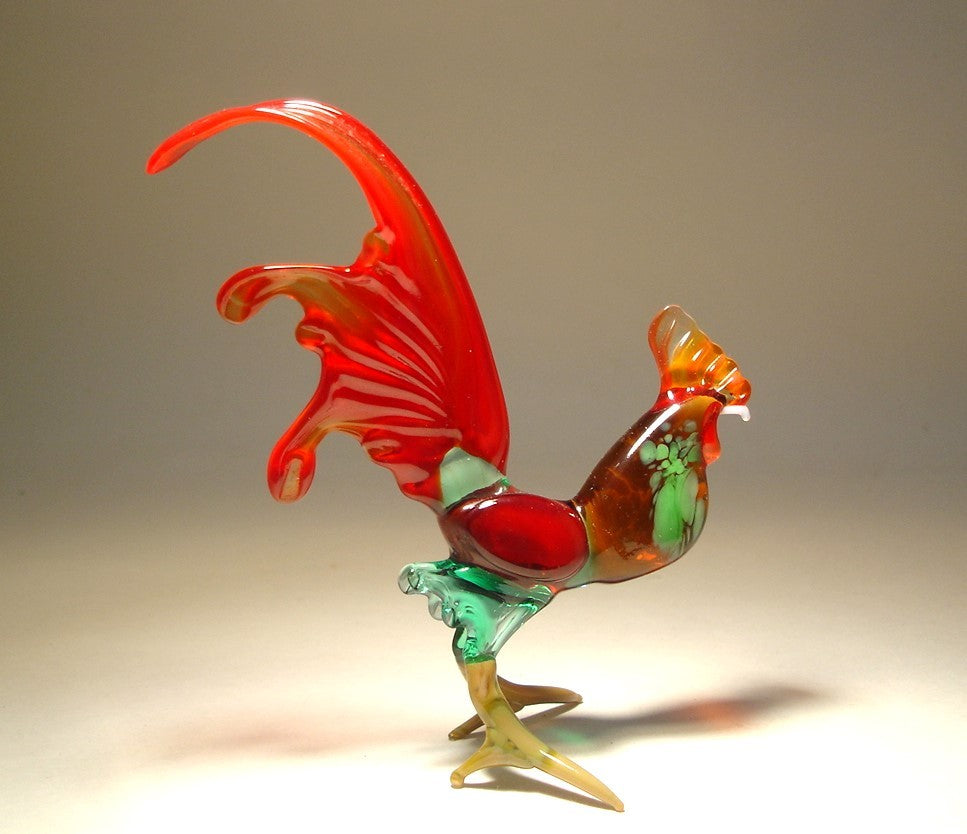 A side view of a glass rooster figurine showcasing its striking red tail feathers, detailed green body, and proud stance.