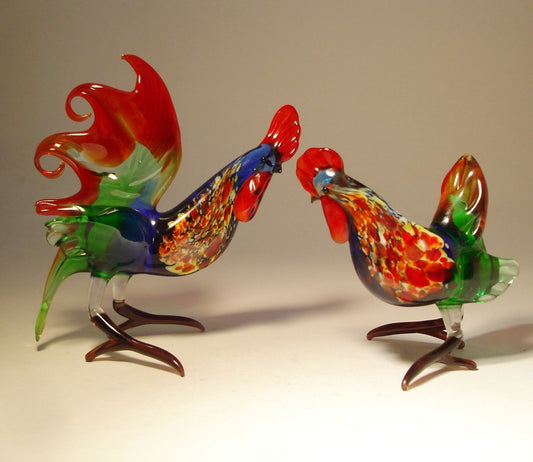 Colorful glass rooster and hen figurines, the rooster is on the left side, the hen is on the right