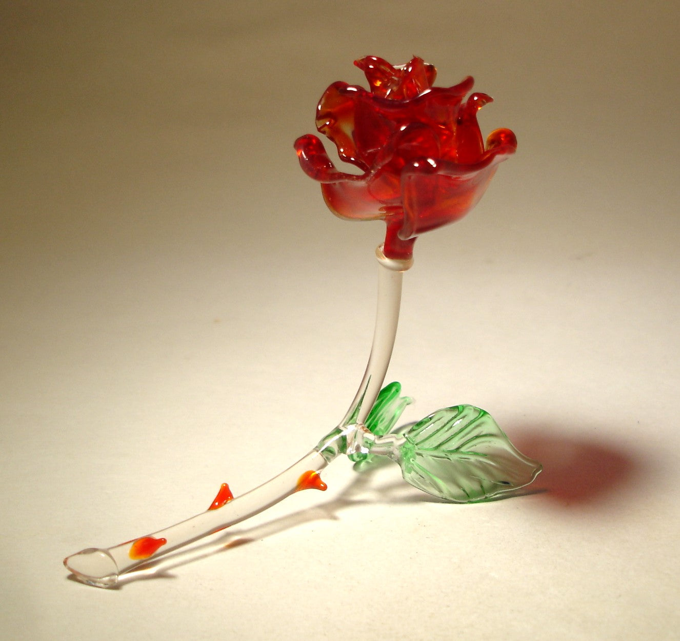 the red glass rose figurine is resting on two green leaves and has a curved stem