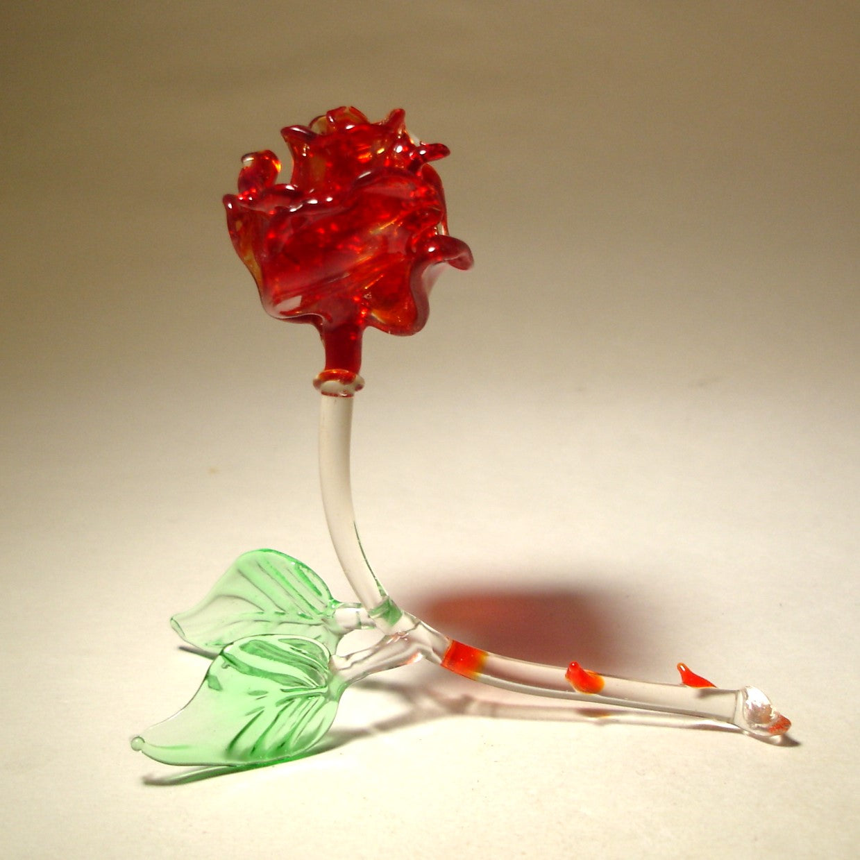 left side view of the dark red glass rose figurine featuring bright red thorns