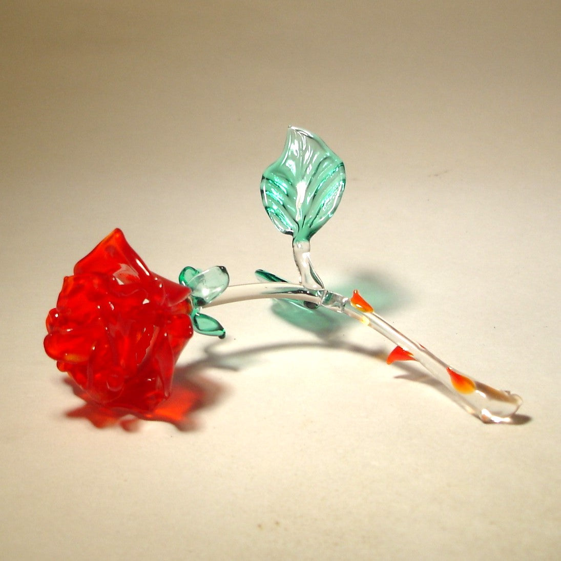 A red rose glass figurine is laying on a side showcasing the details of its beautiful red petals.