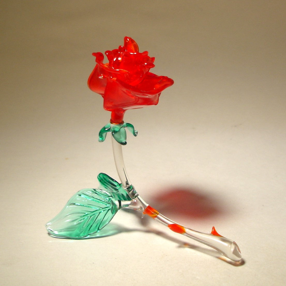 A side view of a red glass rose figurine, showcasing its intricate petals and thorny stem.