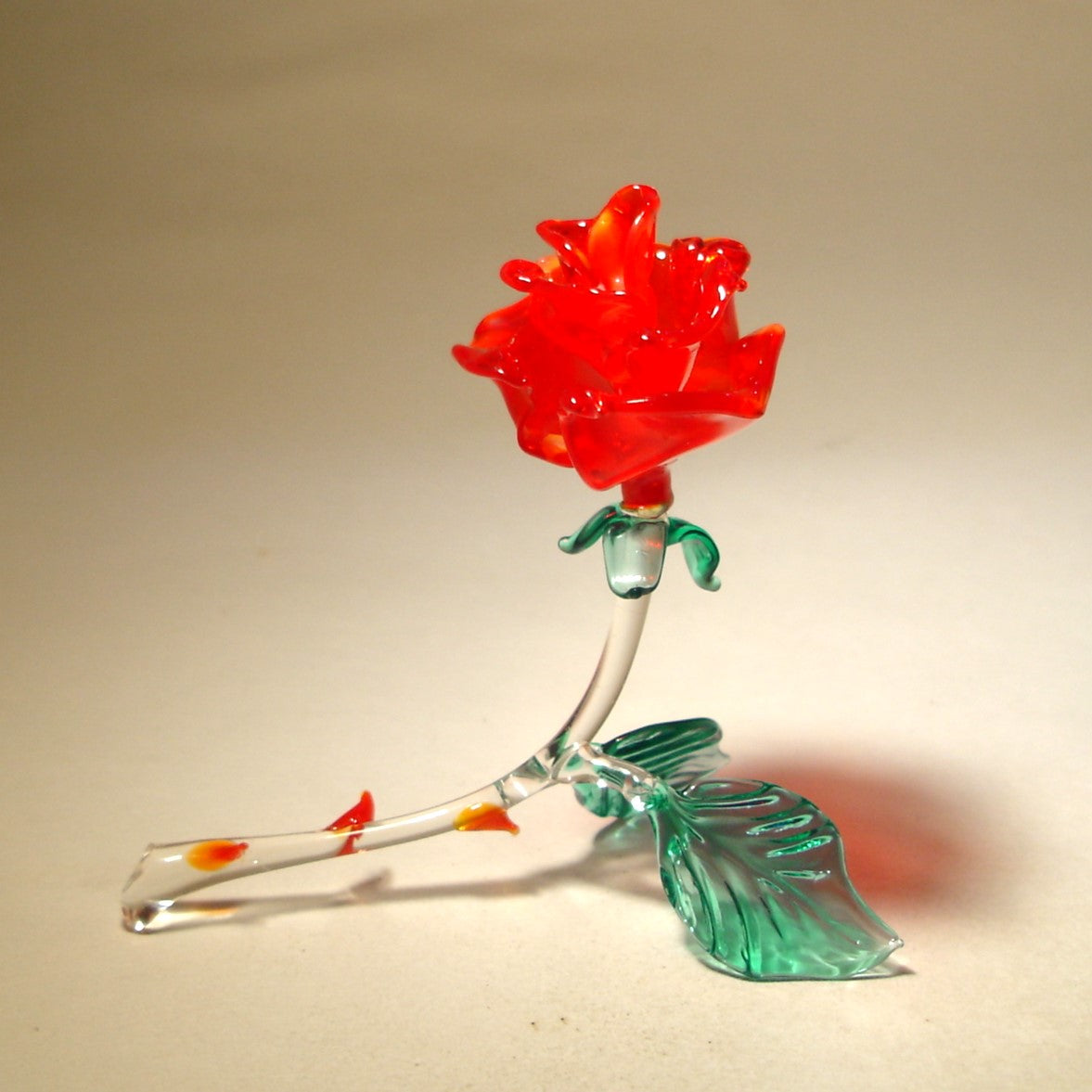 Handcrafted red glass rose figurine with delicate petals, a curved stem adorned with red glass thorns.