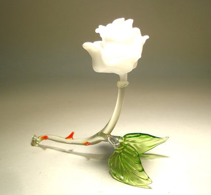 A delicate white glass rose figurine with intricate white petals  resting on two of its green leaves. 