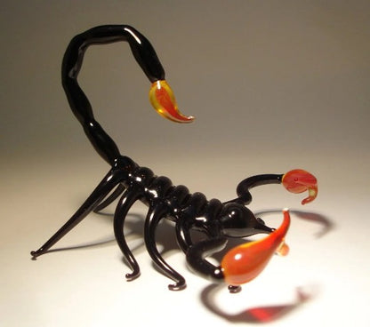 A side view of a black glass scorpion figurine, highlighting its arched tail, a prominent red stinger, and intricate legs.