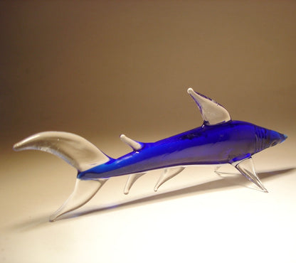 A sleek glass reef shark figurine, displaying a smooth cobalt blue body with a clear glass curved dorsal fin and tail.