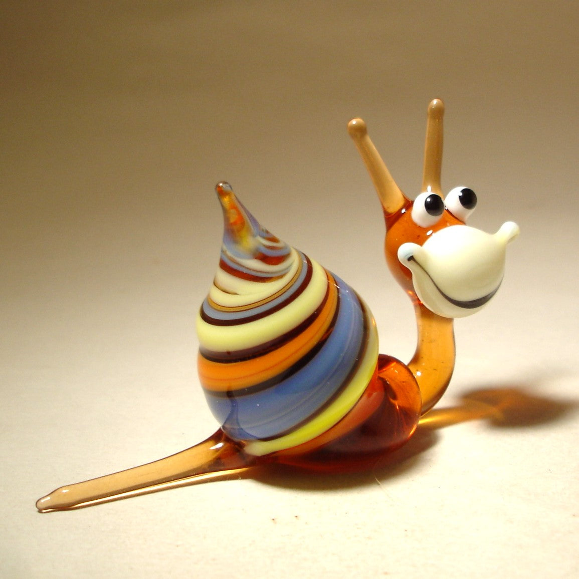 Side view of the Glass Happy Snail Figurine, displaying its colorful spiral shell as it appears to crawl, with its cheerful expression.