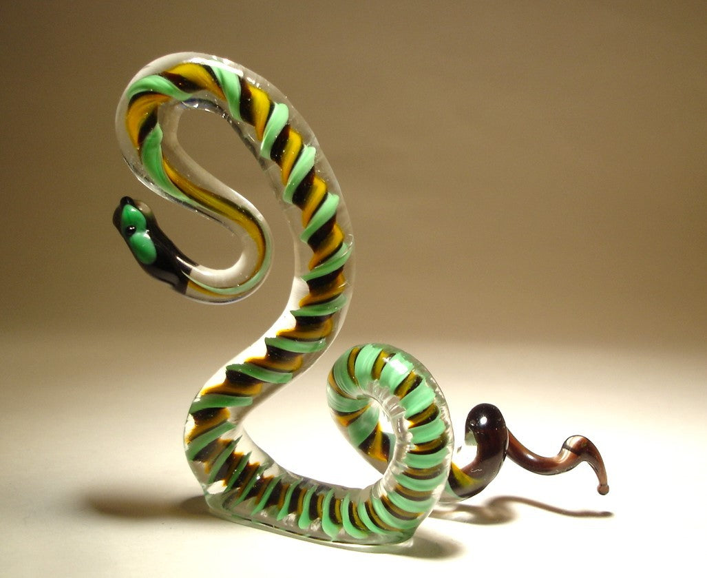 A side view of a glass snake figurine, highlighting its body and intricate pattern of green, black, and yellow, with its head raised and ready to strike.