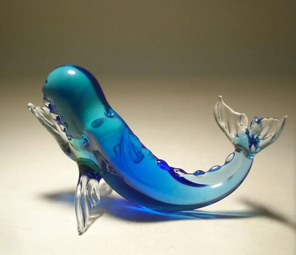 a glass sperm whale figurine, with a raised on the fins blue body and detailed facial features with a semi open jaw.