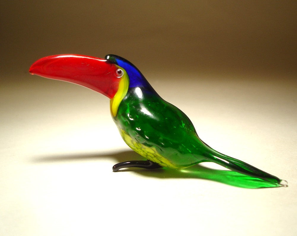  front view of a glass toucan figurine featuring a vibrant red beak, showcasing its green and yellow body with a blue head.