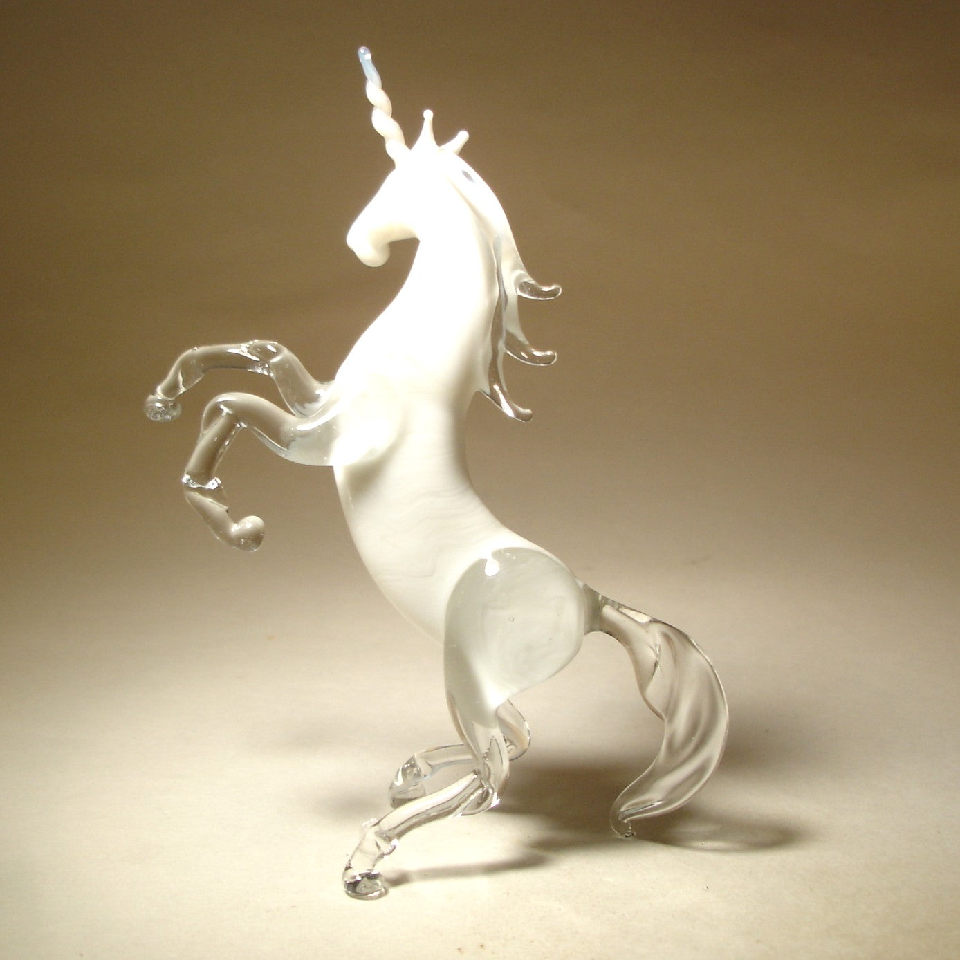 A side view of a glass white unicorn figurine, emphasizing its elegant posture and the intricate design of its flowing mane and tail