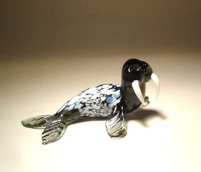 A front view of a glass walrus figurine, showcasing its long tusks, detailed facial features, and smooth body, with a slightly curved pose that captures the essence of the walrus.