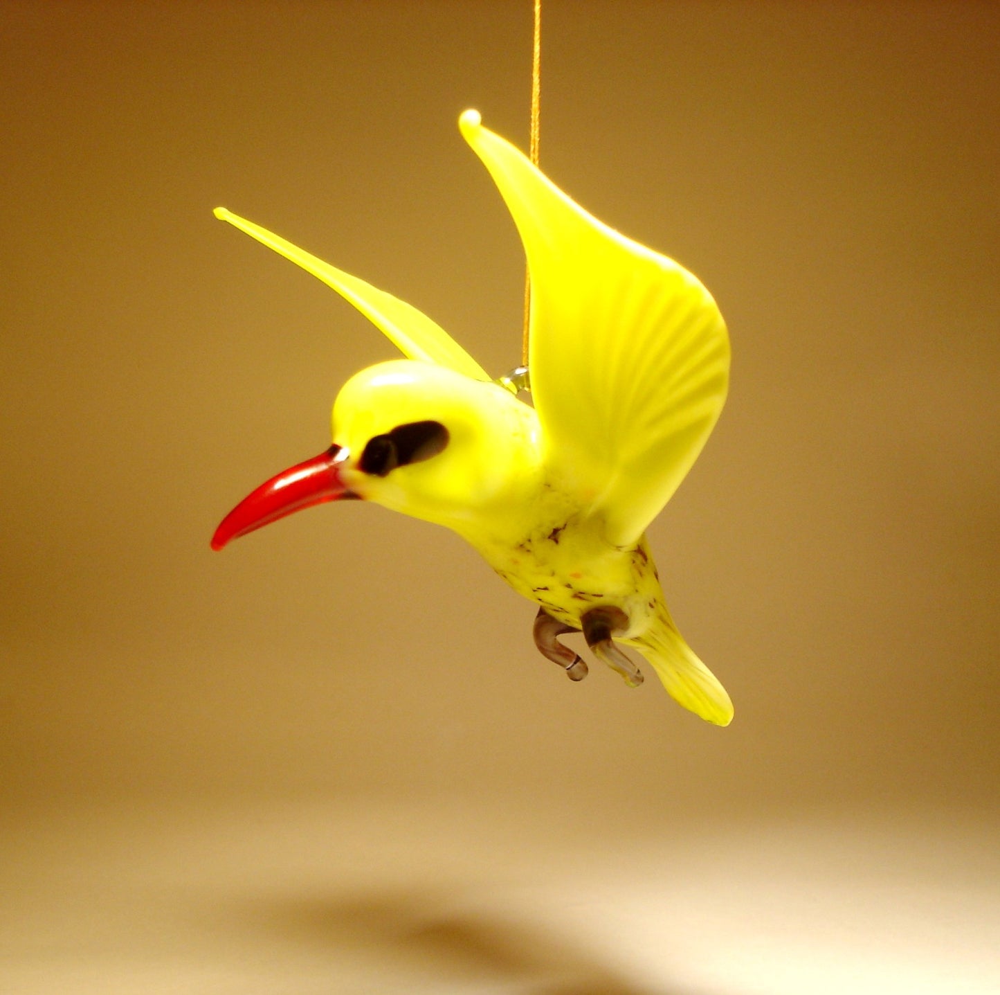 Side view of the yellow glass bird ornament, highlighting its graceful posture and smooth curves, suspended from a string.