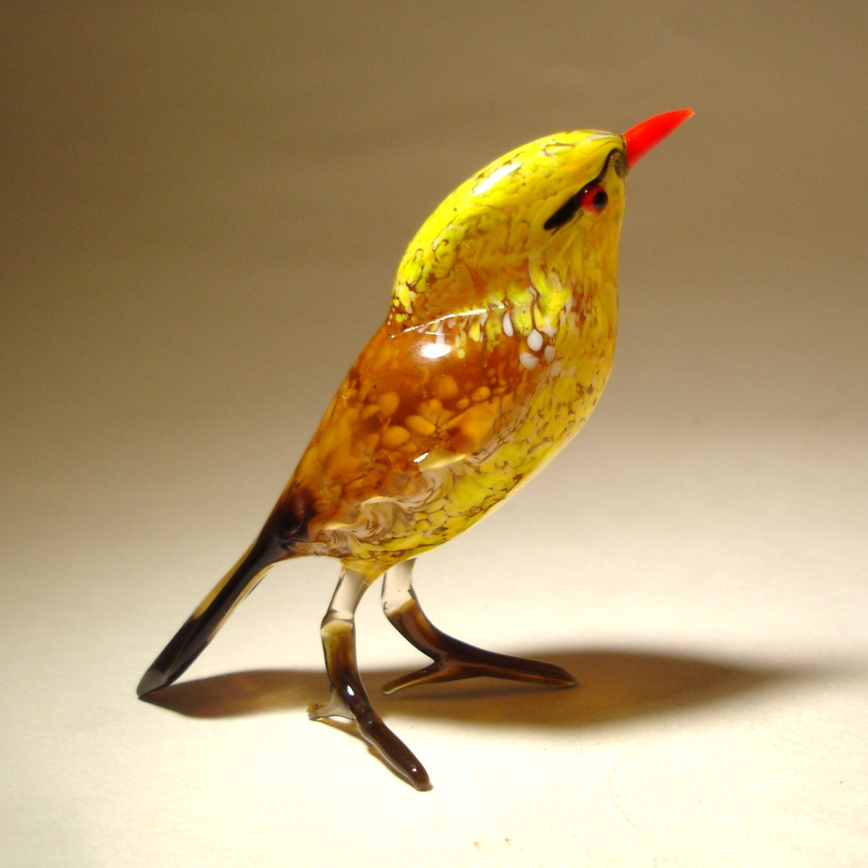 A side view of the yellow glass bird figurine, highlighting its elegant silhouette, the contrast between the vivid yellow body and the striking red beak.