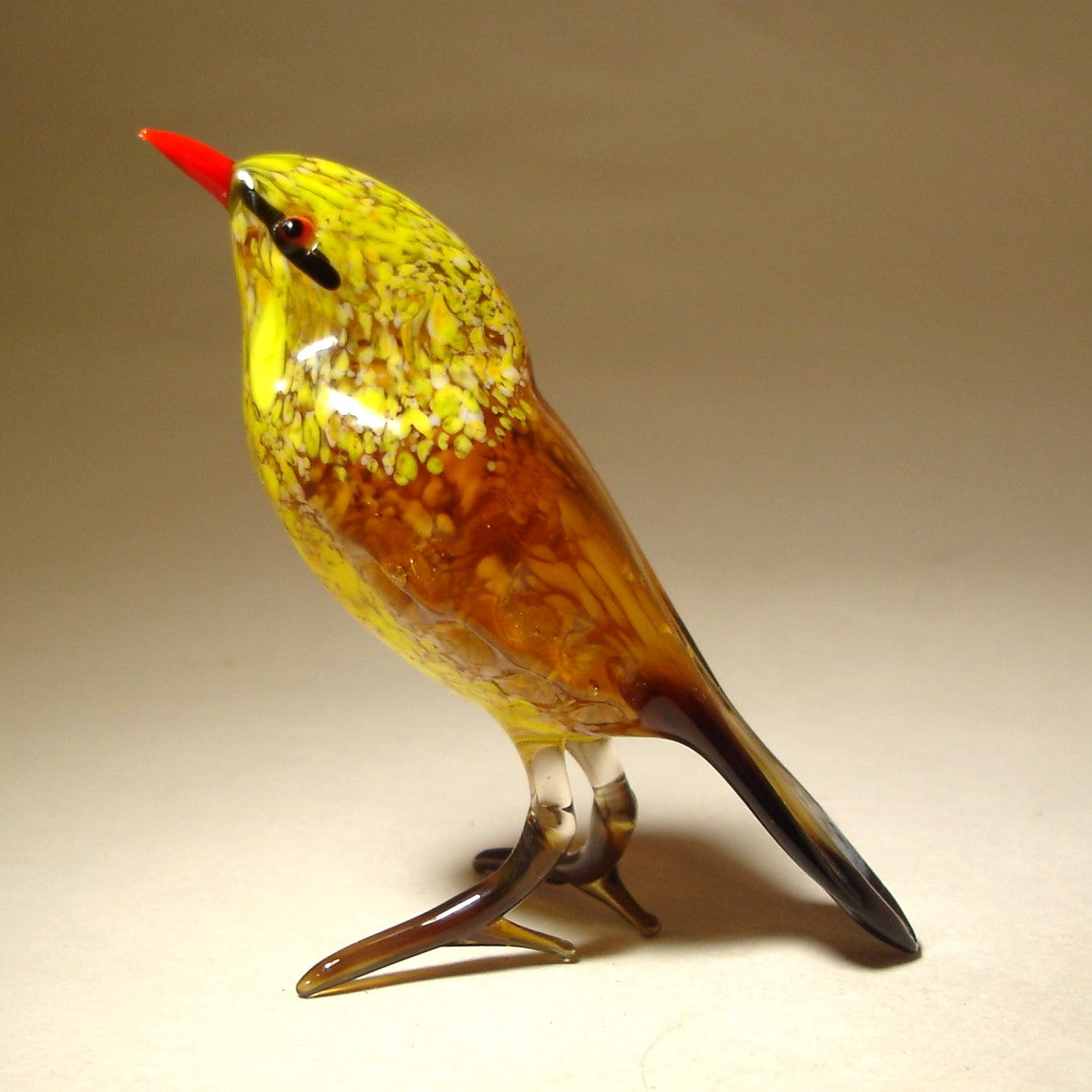 A front view of a yellow glass bird figurine featuring a bright red beak, showcasing its smooth body, detailed eyes, and a cheerful expression.