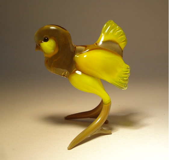 Side view of a handmade glass chicken figurine with bright yellow wings and tail and translucent light brown body and head.