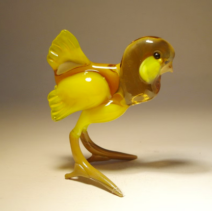 Close-up of a cheerful yellow glass chicken figurine, showcasing its  intricate detailing  of the beak, cheeks and wings. 