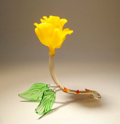 A side view of the yellow rose glass figurine, highlighting the layered petals as they gently open from the center. The transparent green stem curves naturally, supporting the flower.