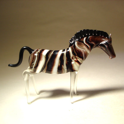 A side profile of the glass zebra figurine, displaying its elongated body and gracefully arched neck and black short mane.