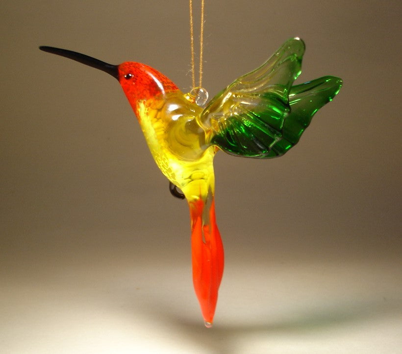 A bright yellow glass hummingbird ornament suspended in mid-air, featuring intricate details on its wings and tail.