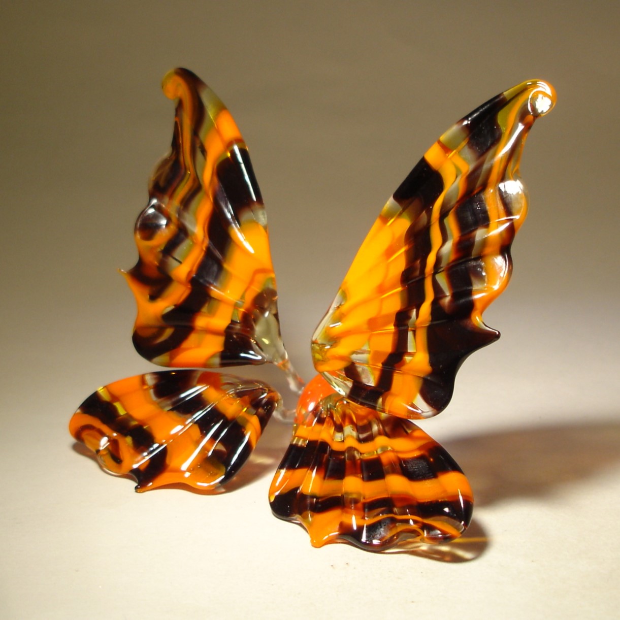 A side profile of the orange and black glass butterfly figurine, showcasing its gently arched wings and orange body. 