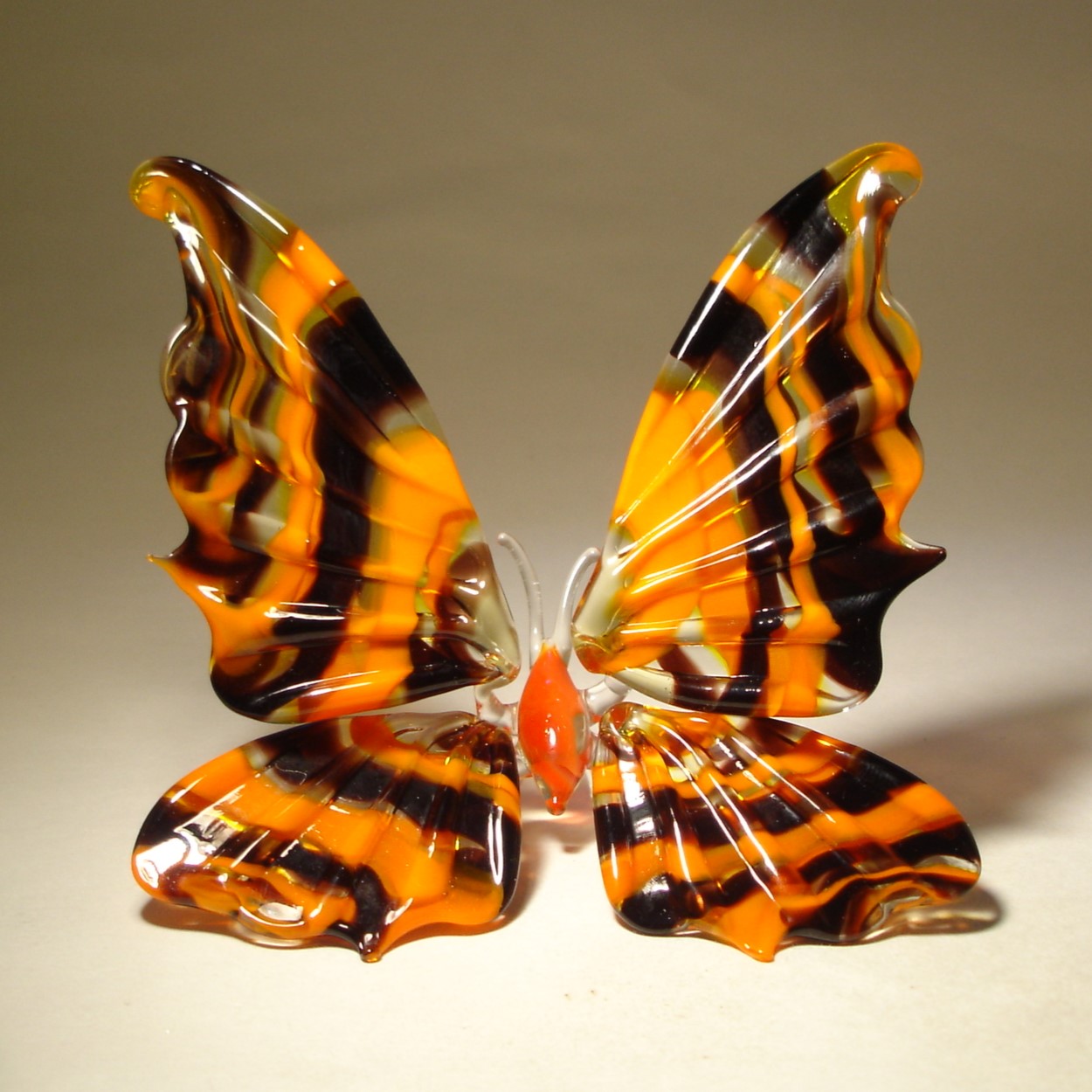 A glass figurine of a butterfly with vibrant orange and black striped wings, delicately spread out.